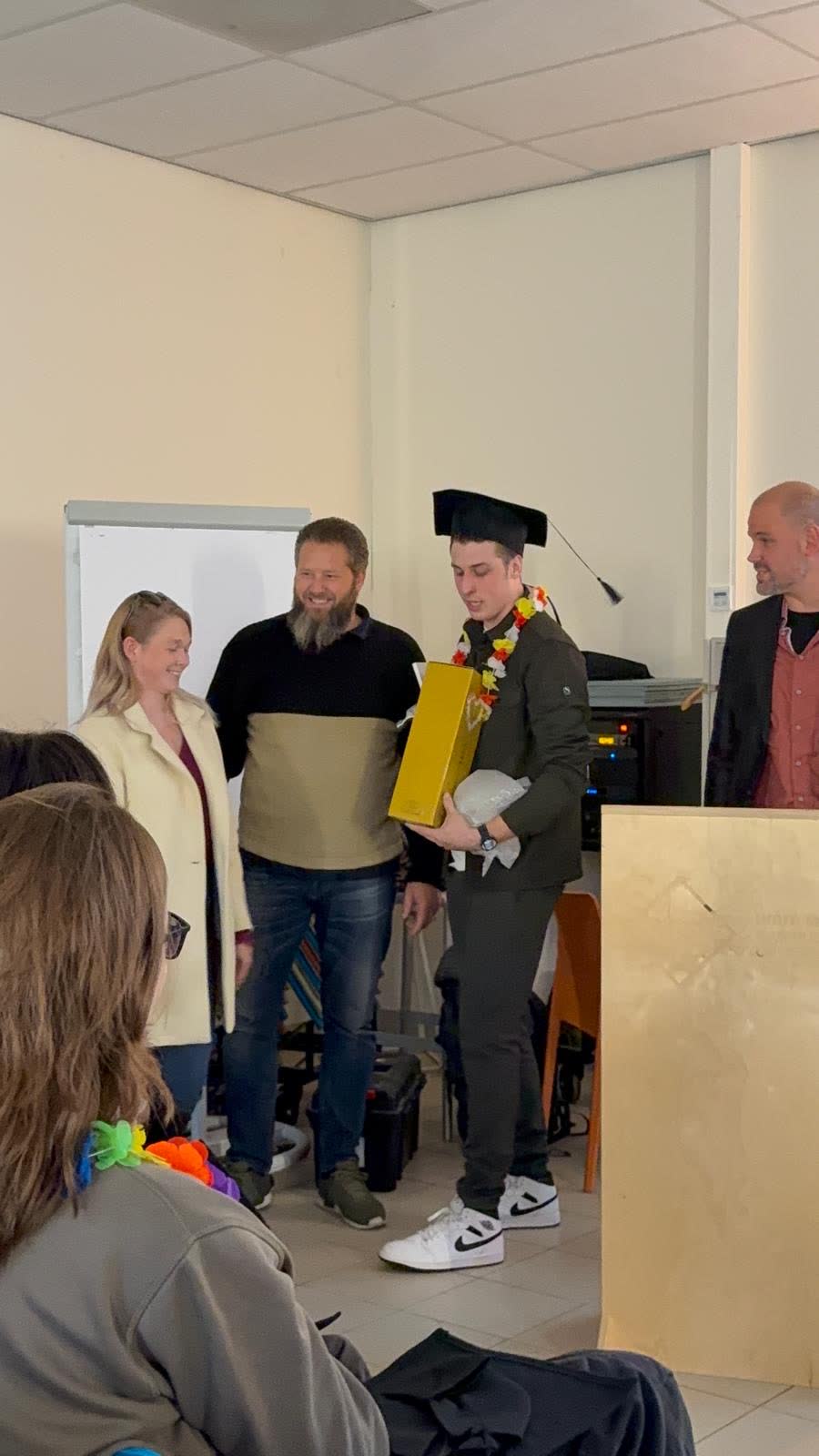 Onze leerling krijgt zijn diploma, met de baret op en Herman ernaast